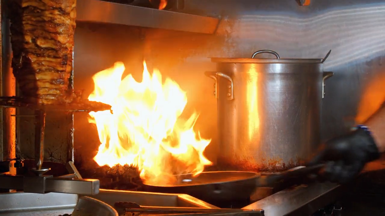 Flames leaping from the grill beside the shawarma spit